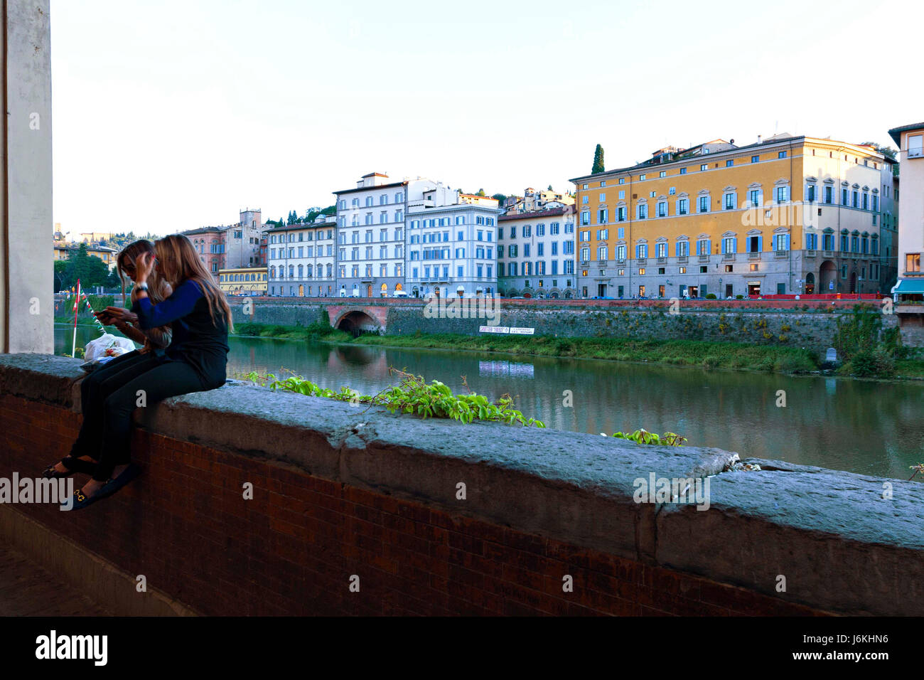 2 giovane donna seduta sulla parete presso il fiume Arno, Firenze, Italia Foto Stock