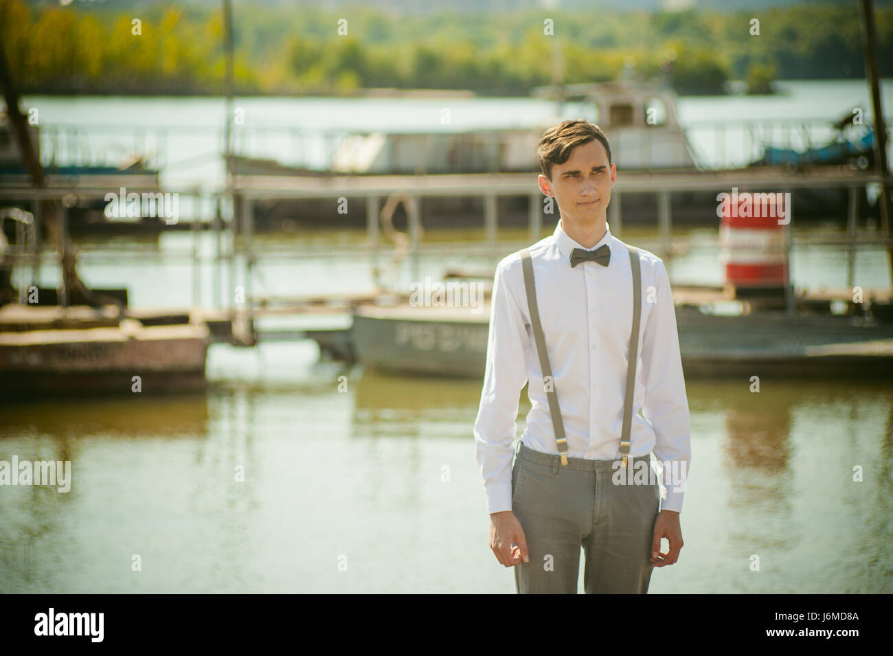 Giovane uomo magro, elegantemente vestito elegantemente in una camicia  bianca, grigio pantaloni con bretelle e il filtro bow tie. Ritratto giovane  ragazzo sul molo su sfondo di r Foto stock - Alamy