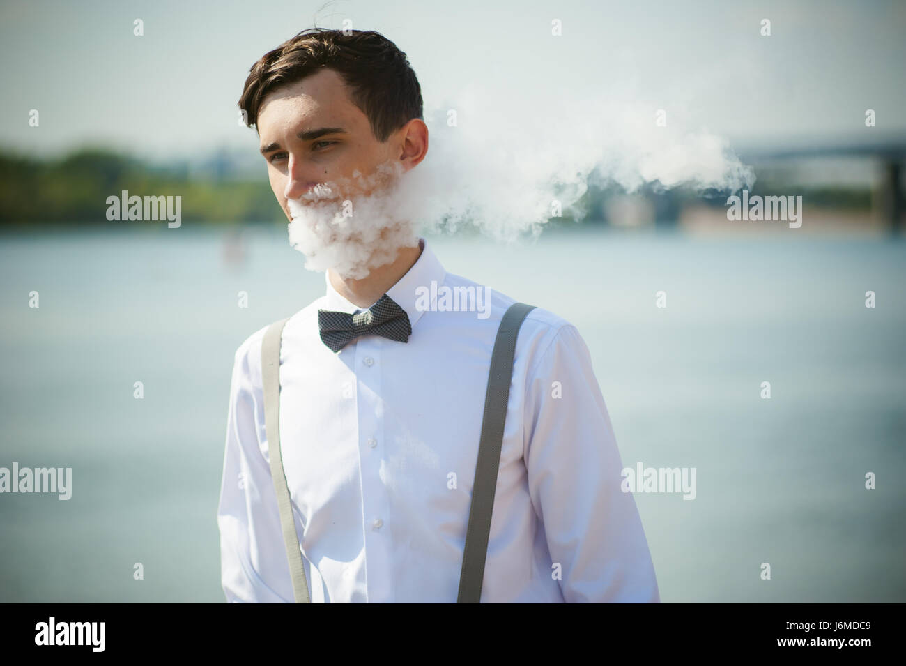 Giovane uomo magro, elegantemente vestito elegantemente in una camicia  bianca, pantaloni con bretelle e il filtro bow tie. vaper guy fuma una  e-sigaretta, releas vapori di Foto stock - Alamy