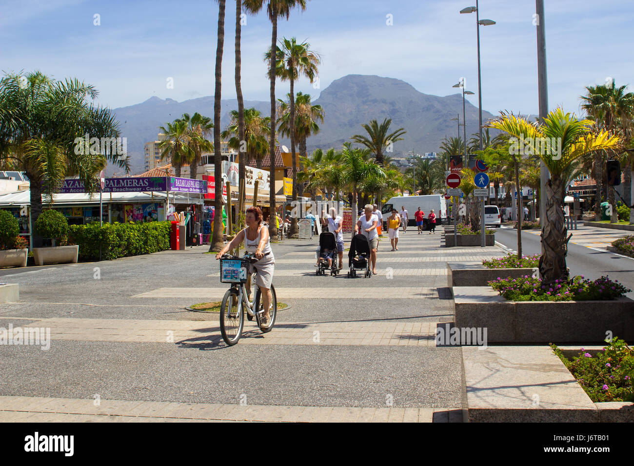 I turisti a piedi e in bicicletta su un viale alberato con negozi e caffetterie in Playa de Las Americas sull isola di Teneriffe Foto Stock