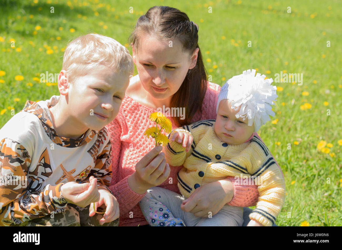 Mamma e figlia e un Figlio seduto sul prato verde con fiori di colore giallo. Foto Stock