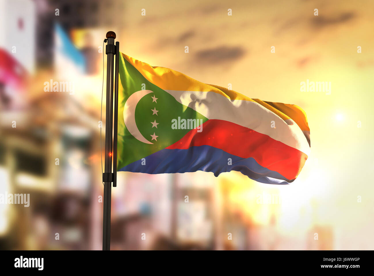 Comore bandiera contro città sfondo sfocato di Sunrise retroilluminazione Foto Stock