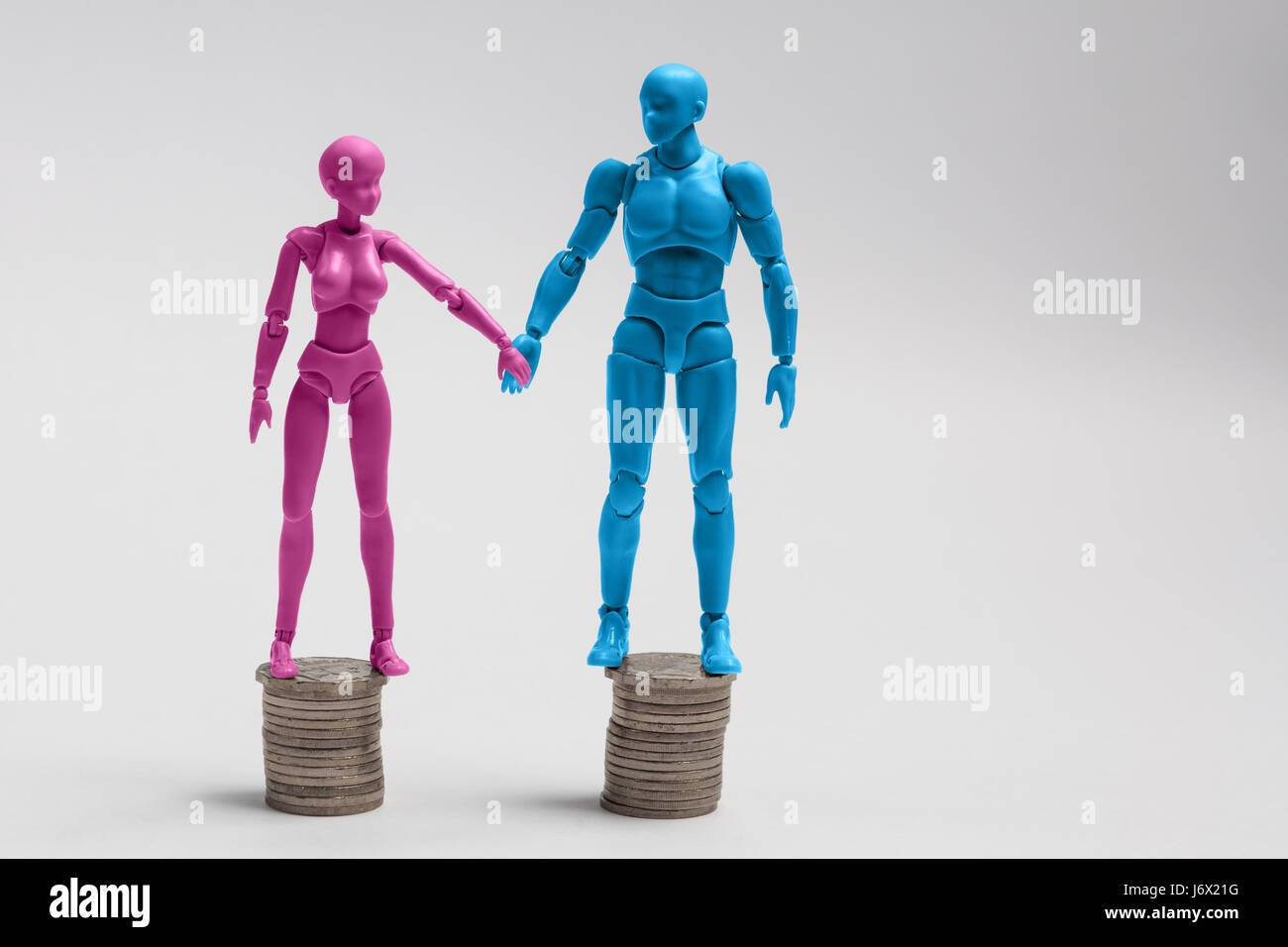 Maschio e femmina figurine tenendo le mani e piedi sulla parte superiore della parità di pile di monete. Reddito il concetto di uguaglianza. Foto Stock