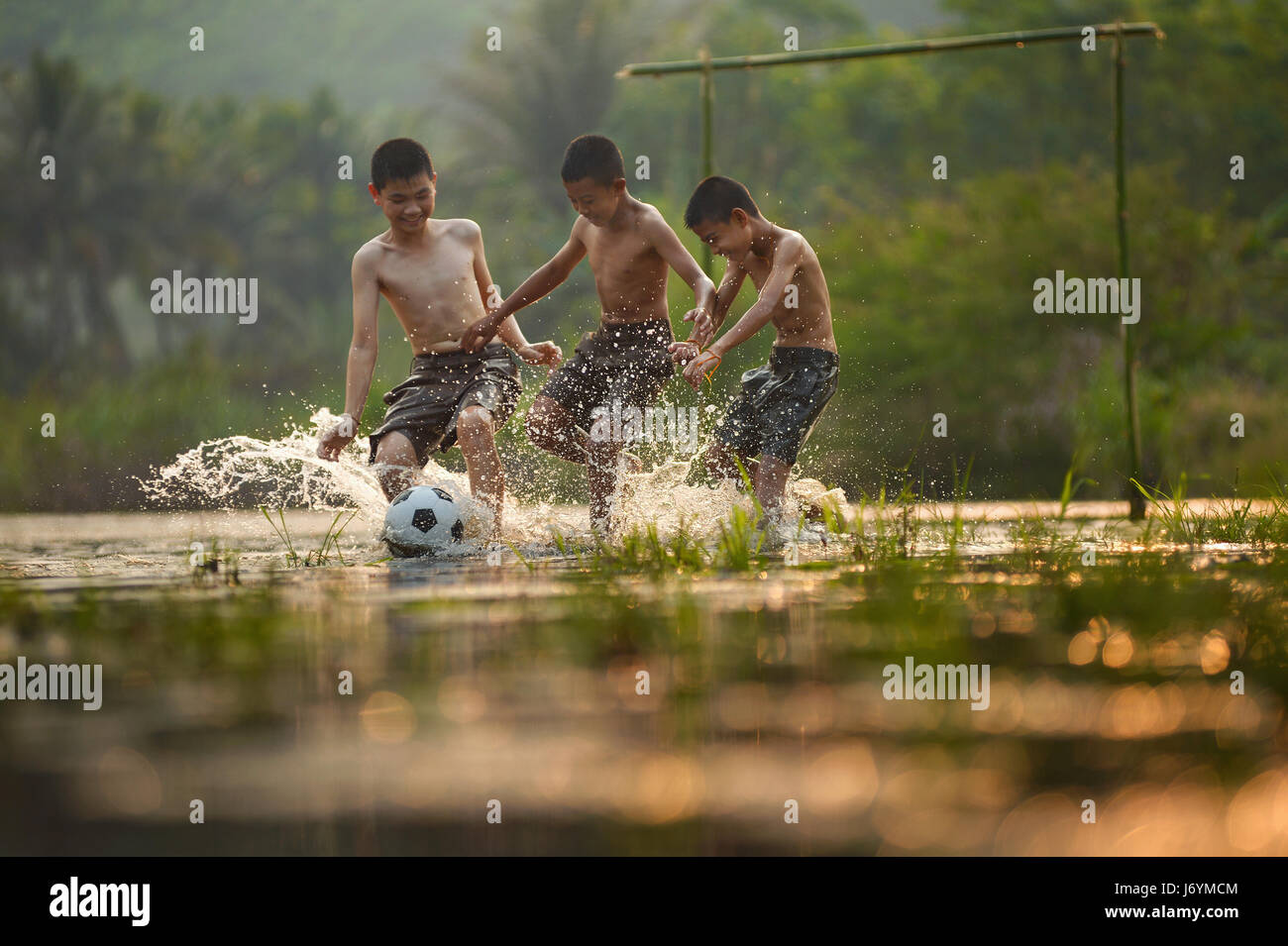 Tre ragazzi che giocano a calcio in un campo saturo di acqua, Thailandia Foto Stock