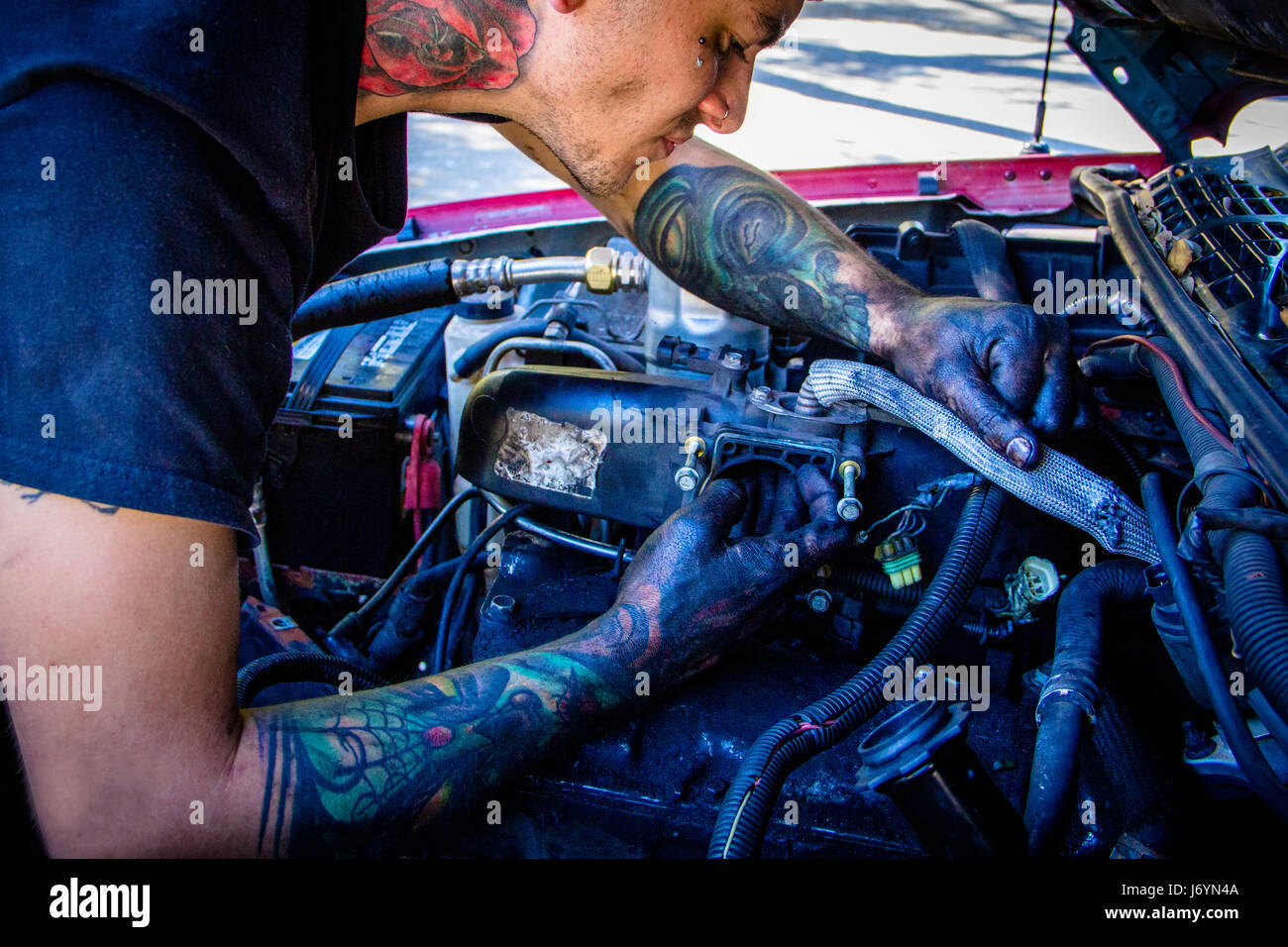 Uomo con tatuaggi lavorando su auto a motore Foto Stock