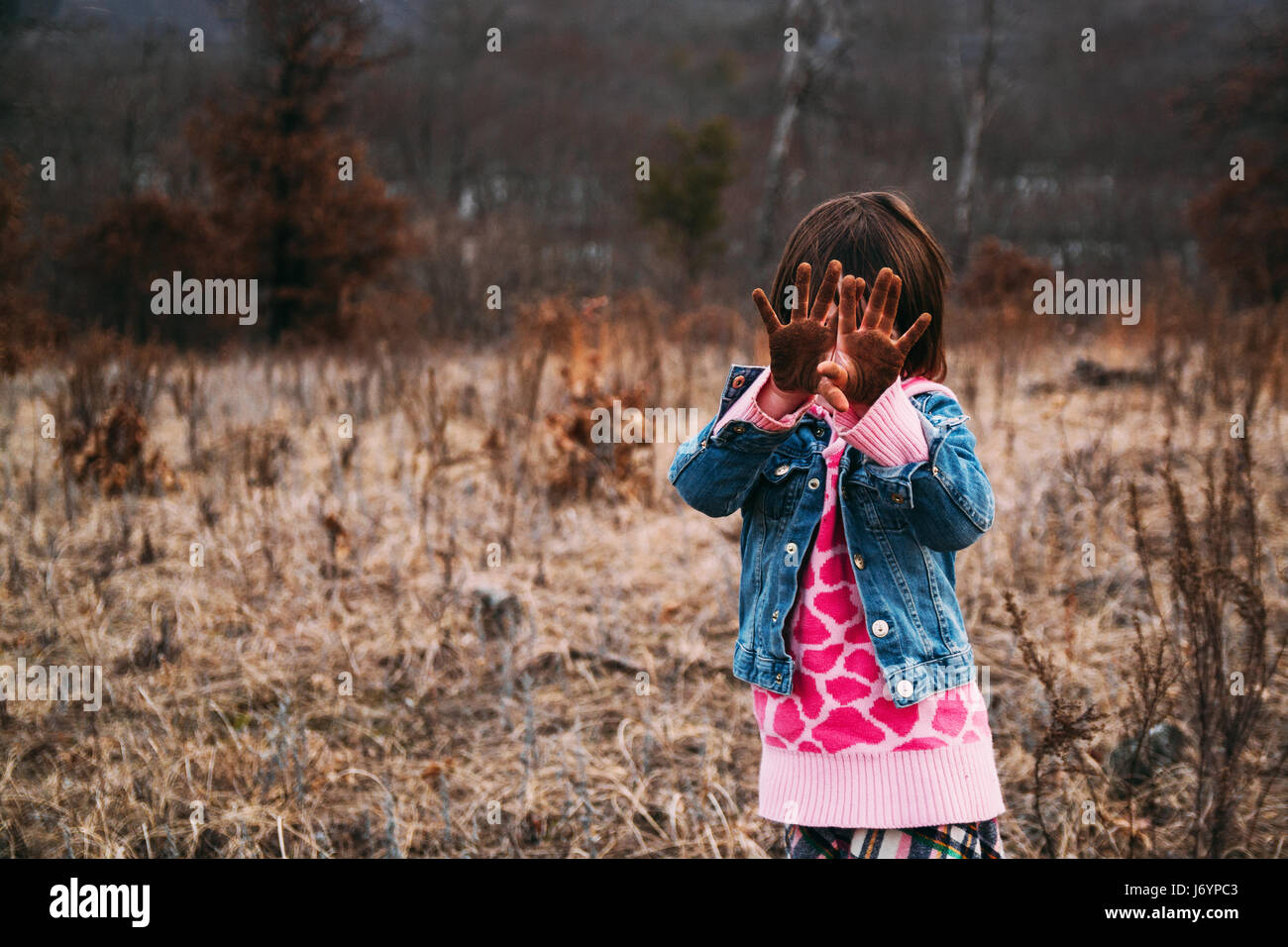 Ragazza in piedi nel paesaggio rurale tenendo le mani sporche di fronte il suo volto Foto Stock