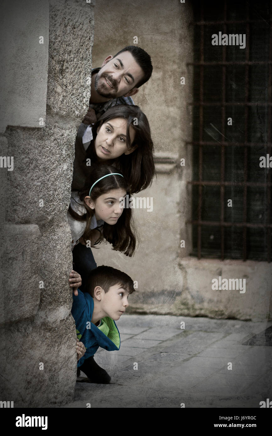 Famiglia spiata dietro l'angolo di un edificio Foto Stock