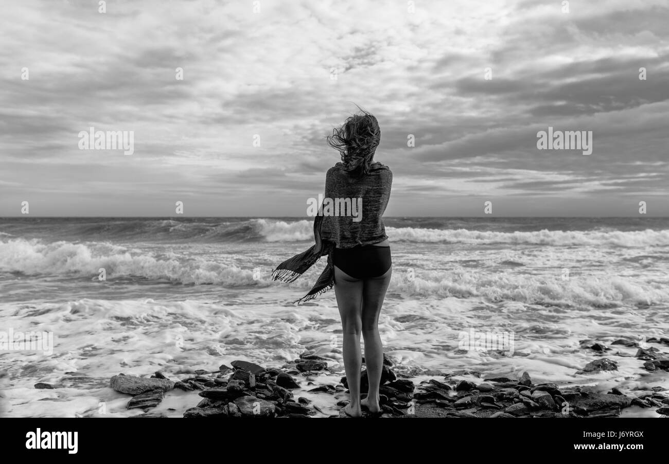 Bianco e nero ritratto di giovane donna attraente in piedi sulla riva con i capelli che soffia nella wint Foto Stock