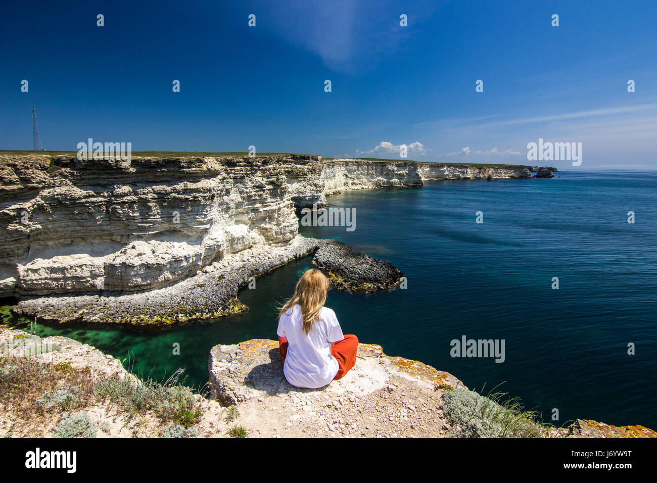 Ragazza in bianco t-seduta breve su una scogliera vicino a Baia Mare Foto Stock