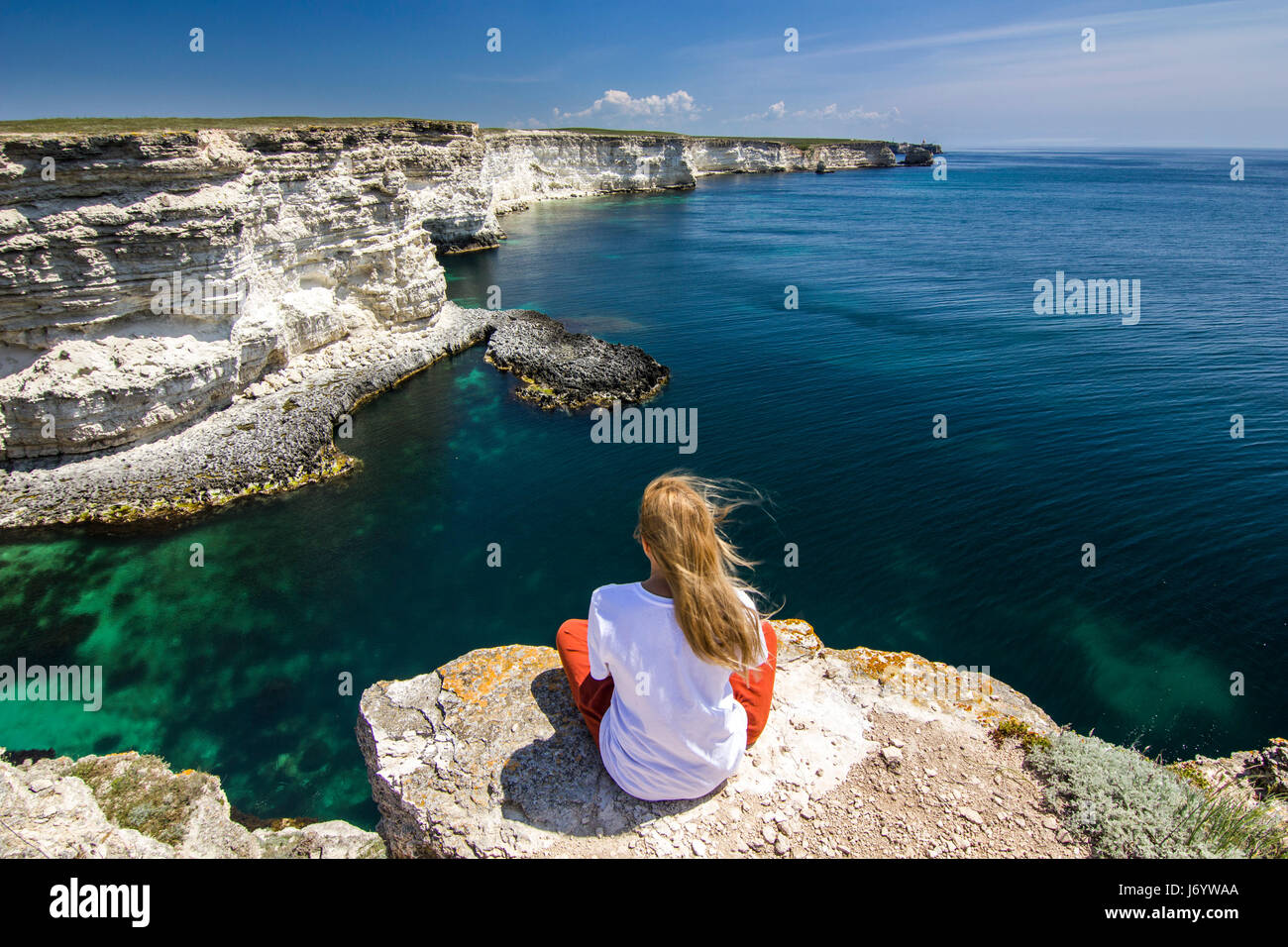 Ragazza in bianco t-seduta breve su una scogliera vicino a Baia Mare Foto Stock