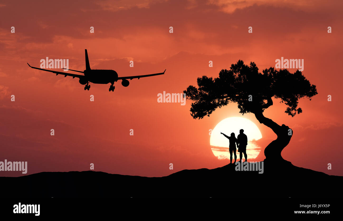 Le persone sotto l'albero storto e aereo sullo sfondo del cielo arancione con sun. Silhouette di un giovane sulla collina, albero, aerei per il trasporto di passeggeri e di Foto Stock