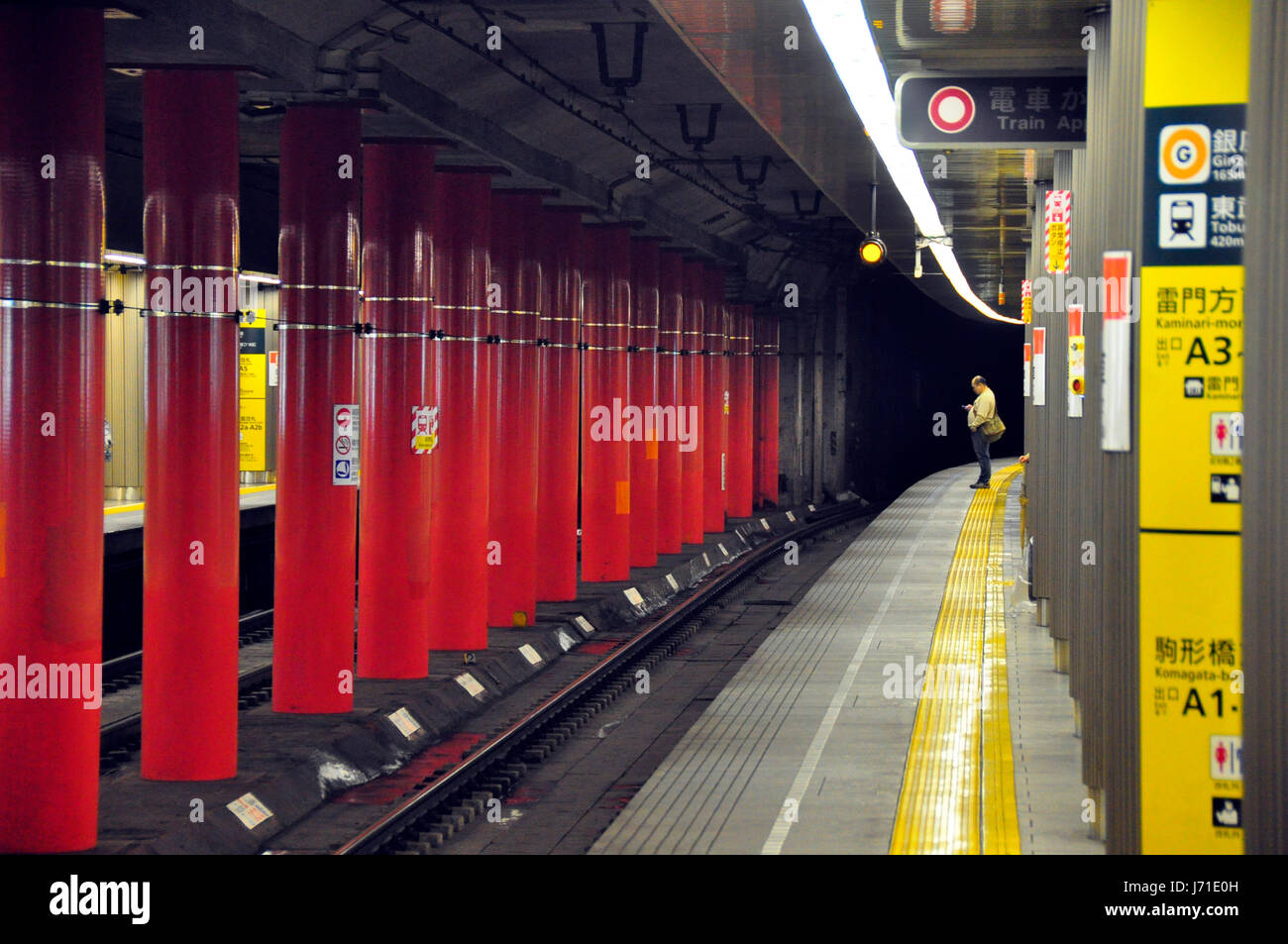 Un uomo solitario controlla il suo telefono come egli si erge su un vuoto che la piattaforma della metropolitana in Giappone, attesa per il prossimo treno. Foto Stock