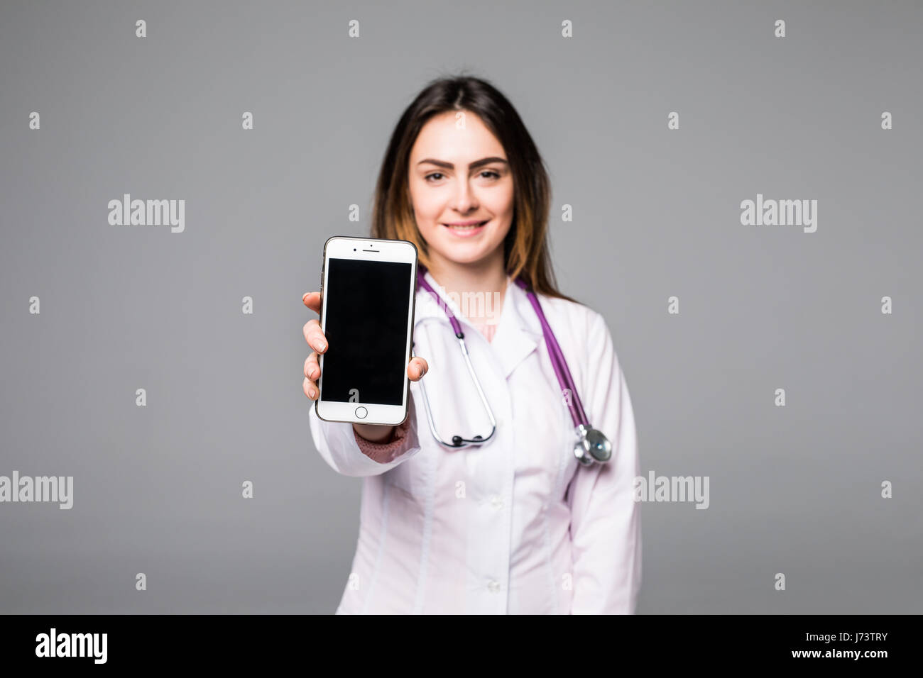 Giovani donne medico mostra telefono mobile contro lo sfondo grigio Foto Stock