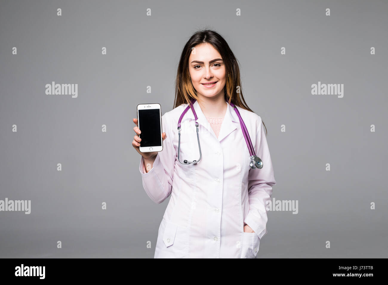 Giovani donne medico mostra telefono mobile contro lo sfondo grigio Foto Stock