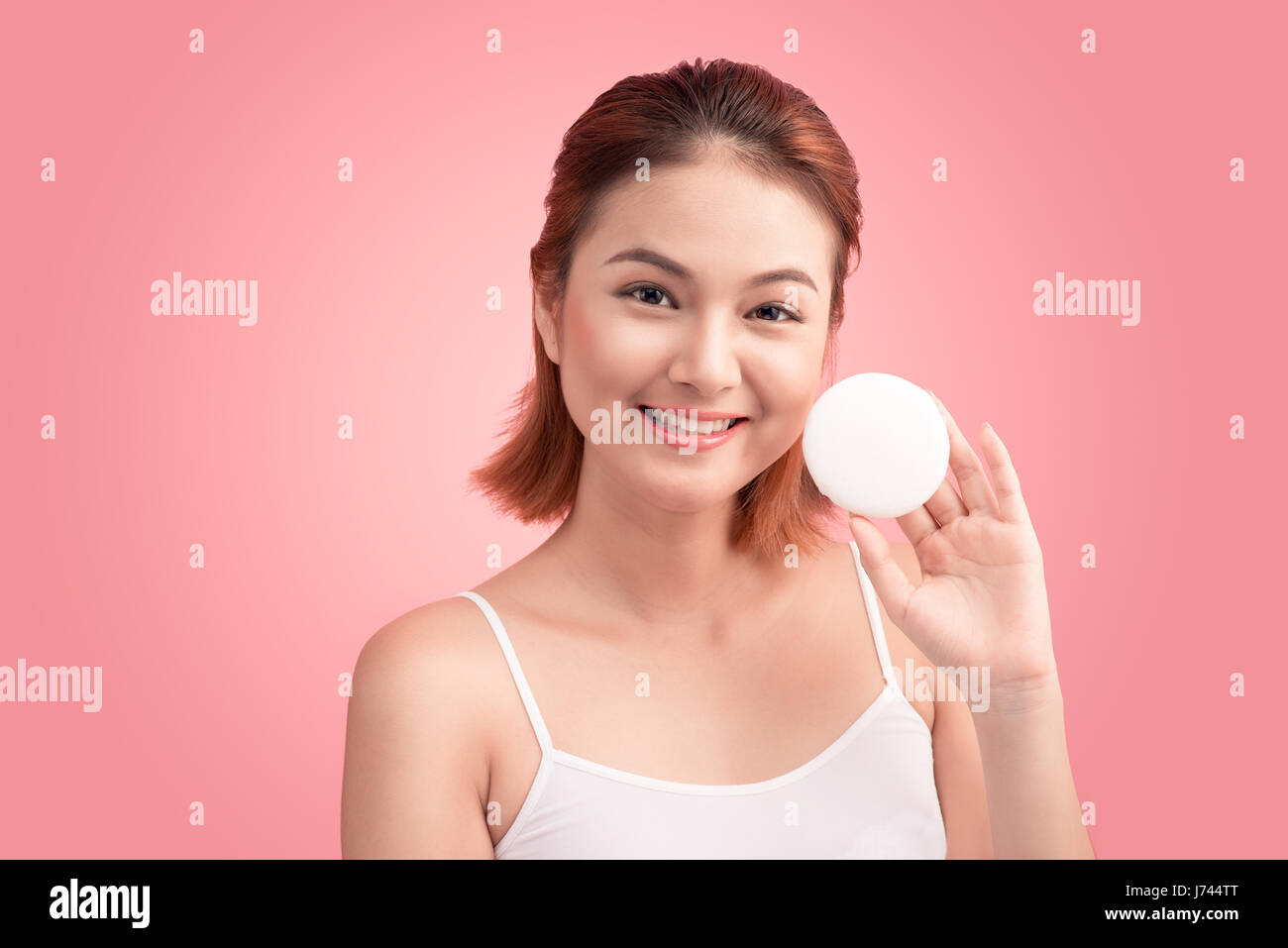 Stupendo giovane donna tenendo premuto il tampone di cotone e sorridente nel prendersi cura del viso per una fresca sana skincare su sfondo rosa Foto Stock