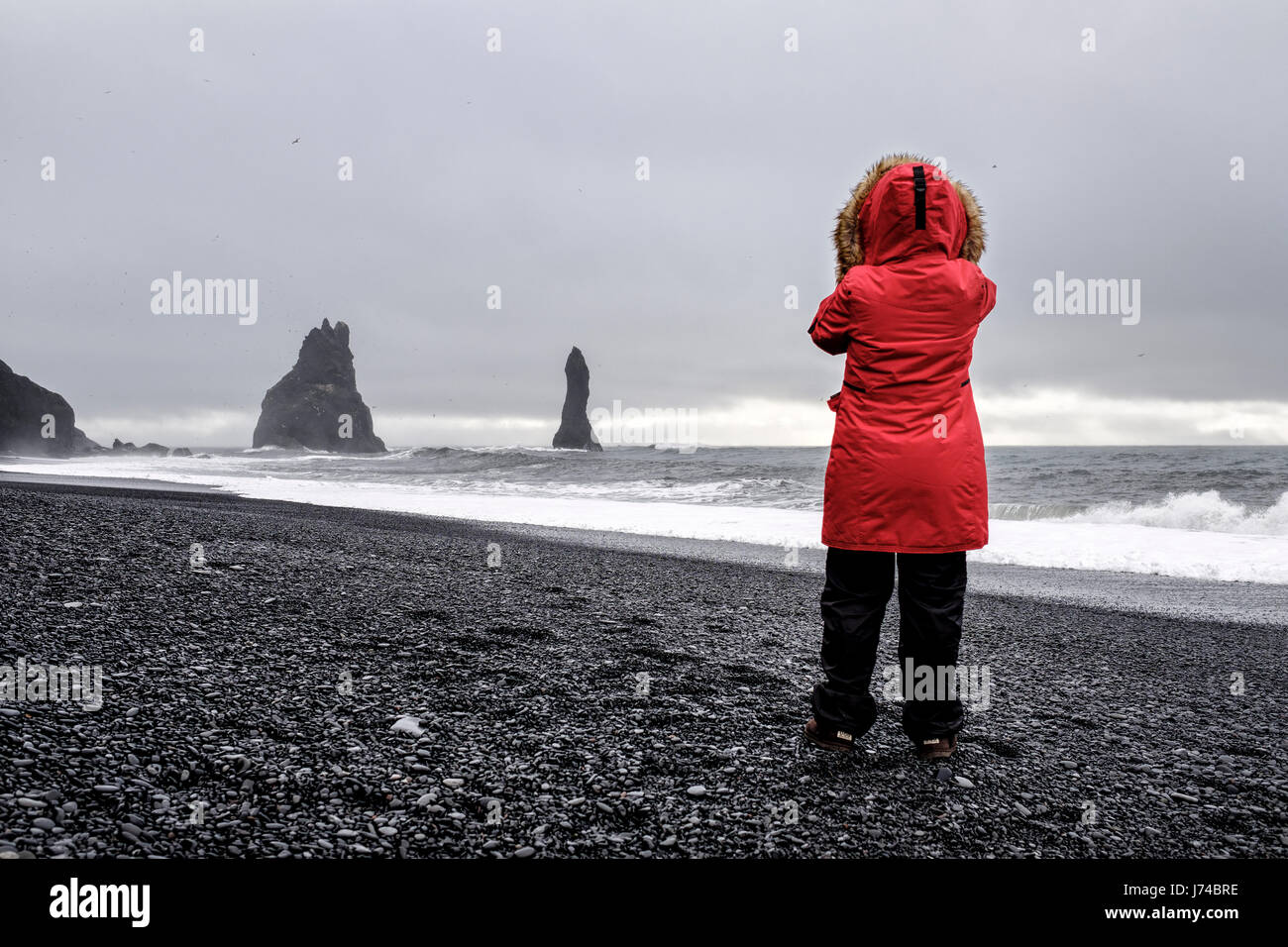 Donna con un cappotto rosso di prendere una fotografia su una spiaggia in un nuvoloso giorno d'inverno. Foto Stock