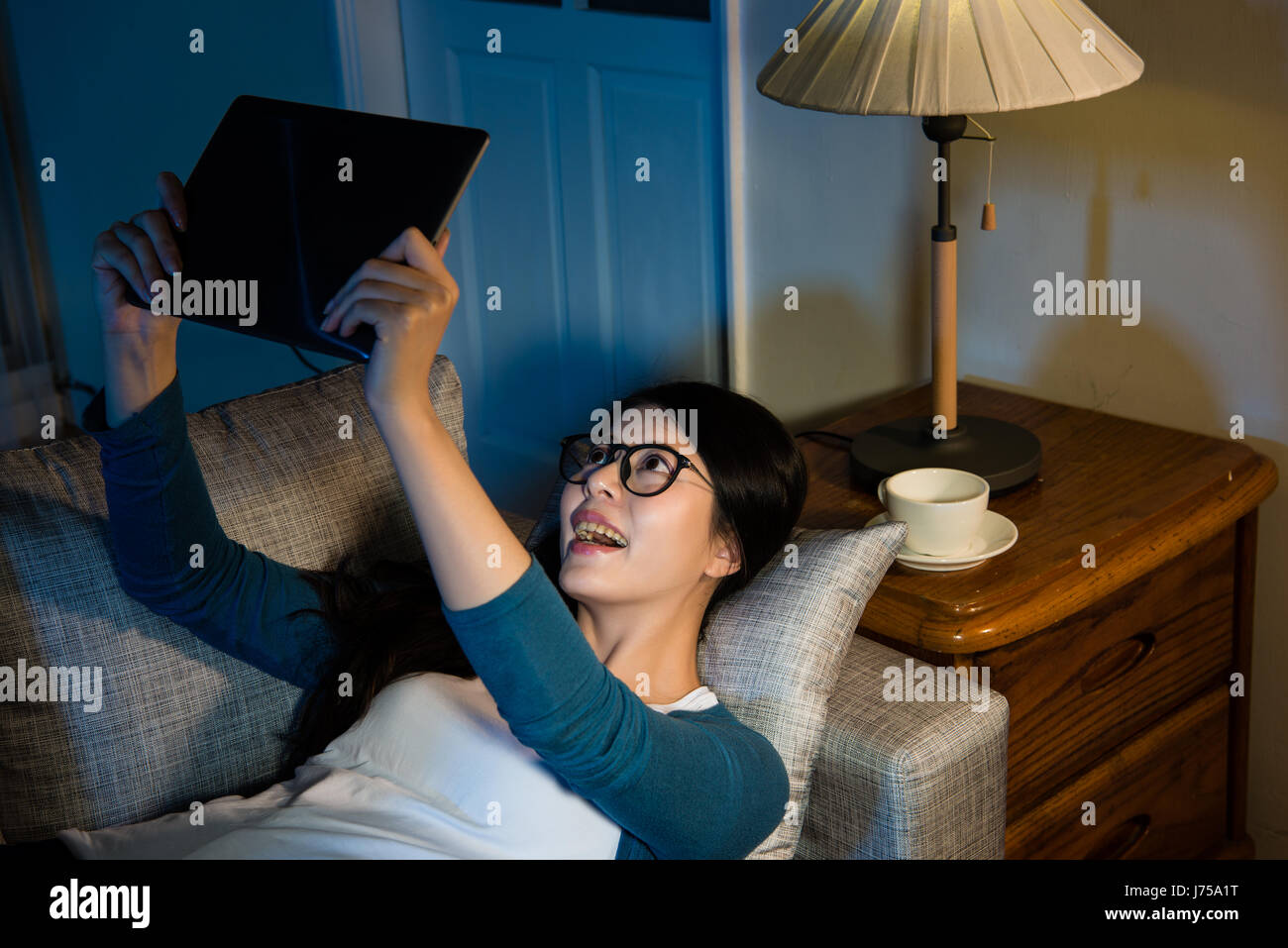 Gara di misto asiatico studente cinese utilizzando big tavoletta digitale computer sdraiato sul divano facetime con la famiglia durante la notte quando si studiano in oltremare Foto Stock