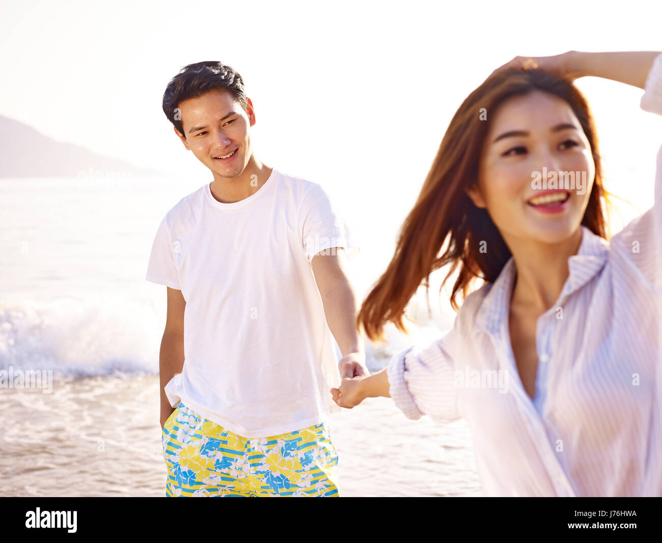 Giovani amorevole e felice coppia asiatica tenendo le mani sulla spiaggia. Foto Stock