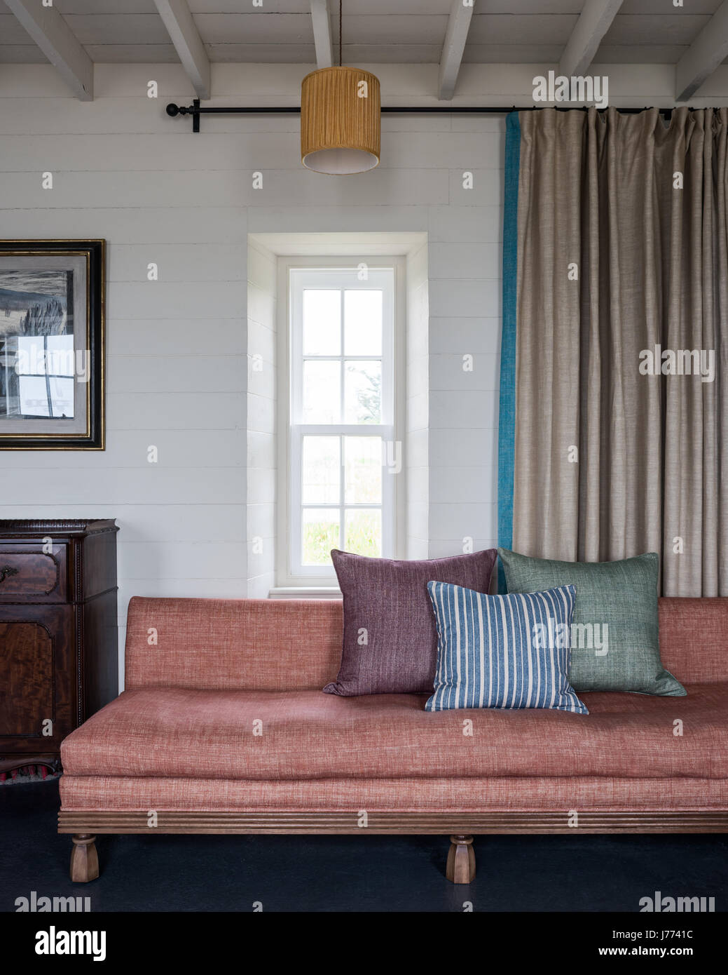 Un assortimento di cuscini sul divano con tende tirate per la massima luce naturale Foto Stock