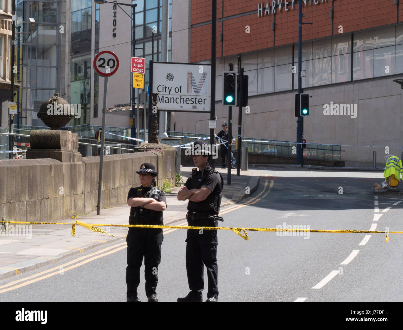 Manchester, Regno Unito. 23 Maggio, 2017. Gli ufficiali di polizia dietro il cordone vicino al Manchester Arena di Manchester City Centre (con Harvey Nichols e una città di Manchester segno visibile), il giorno dopo un attentato suicida ha ucciso 22 come folle sono state lasciando il Ariana Grande concerto presso l'Arena di Manchester. Credito: Chris Rogers/Alamy Live News Foto Stock