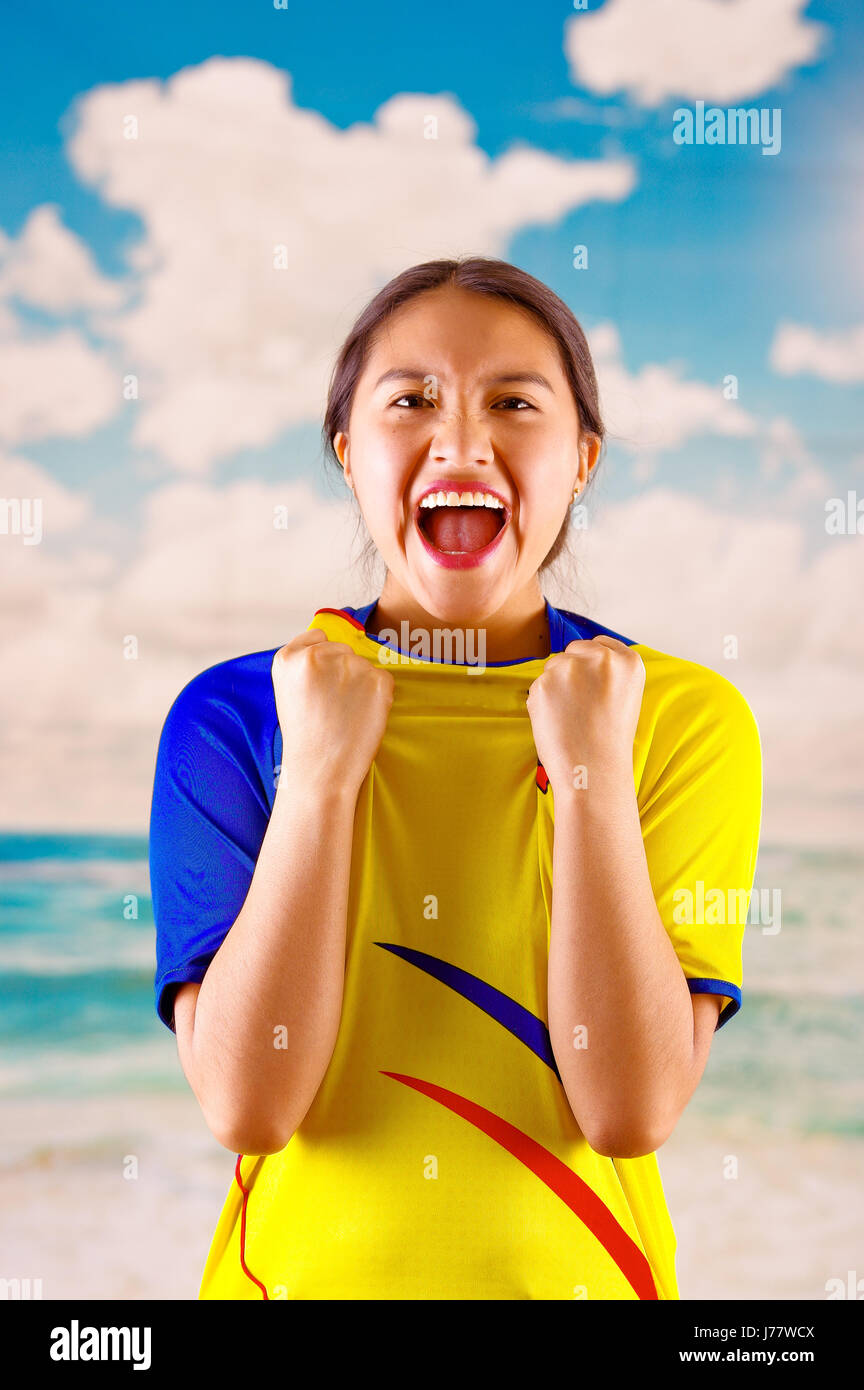 Giovane donna ecuadoriana indossando maratona ufficiale Football Shirt in piedi di fronte alla fotocamera, molto impegnato il linguaggio del corpo la visione di gioco con grande entusiasmo, cielo blu e nuvole sullo sfondo Foto Stock