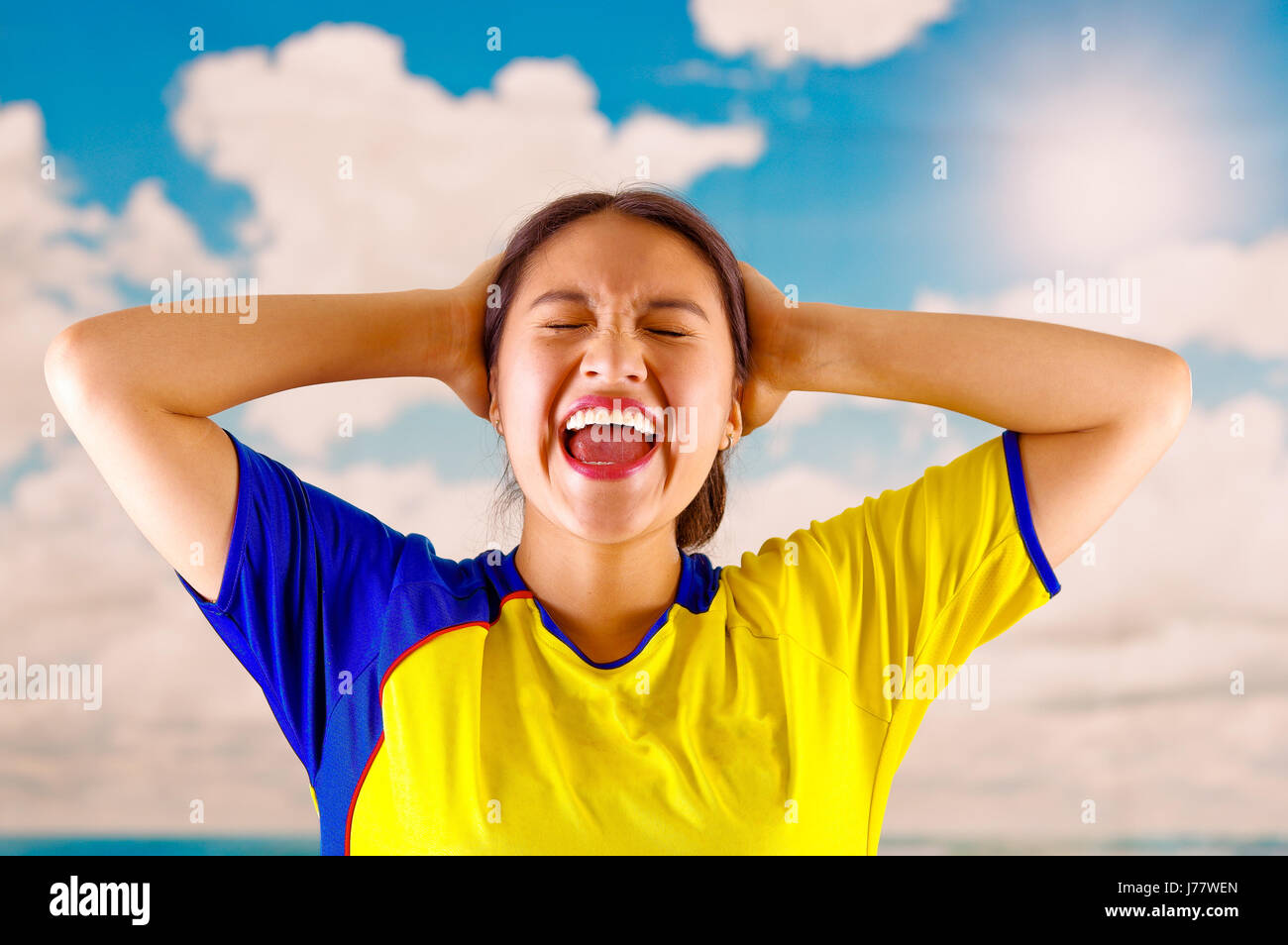 Giovane donna ecuadoriana indossando maratona ufficiale Football Shirt in piedi di fronte alla fotocamera, molto impegnato il linguaggio del corpo la visione di gioco con grande entusiasmo, cielo blu e nuvole sullo sfondo Foto Stock