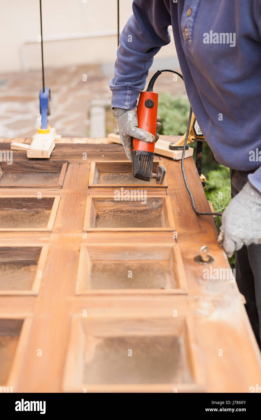 Carpenter al lavoro con la smerigliatrice angolare. La manutenzione e il restauro di una vecchia porta di legno. Foto Stock