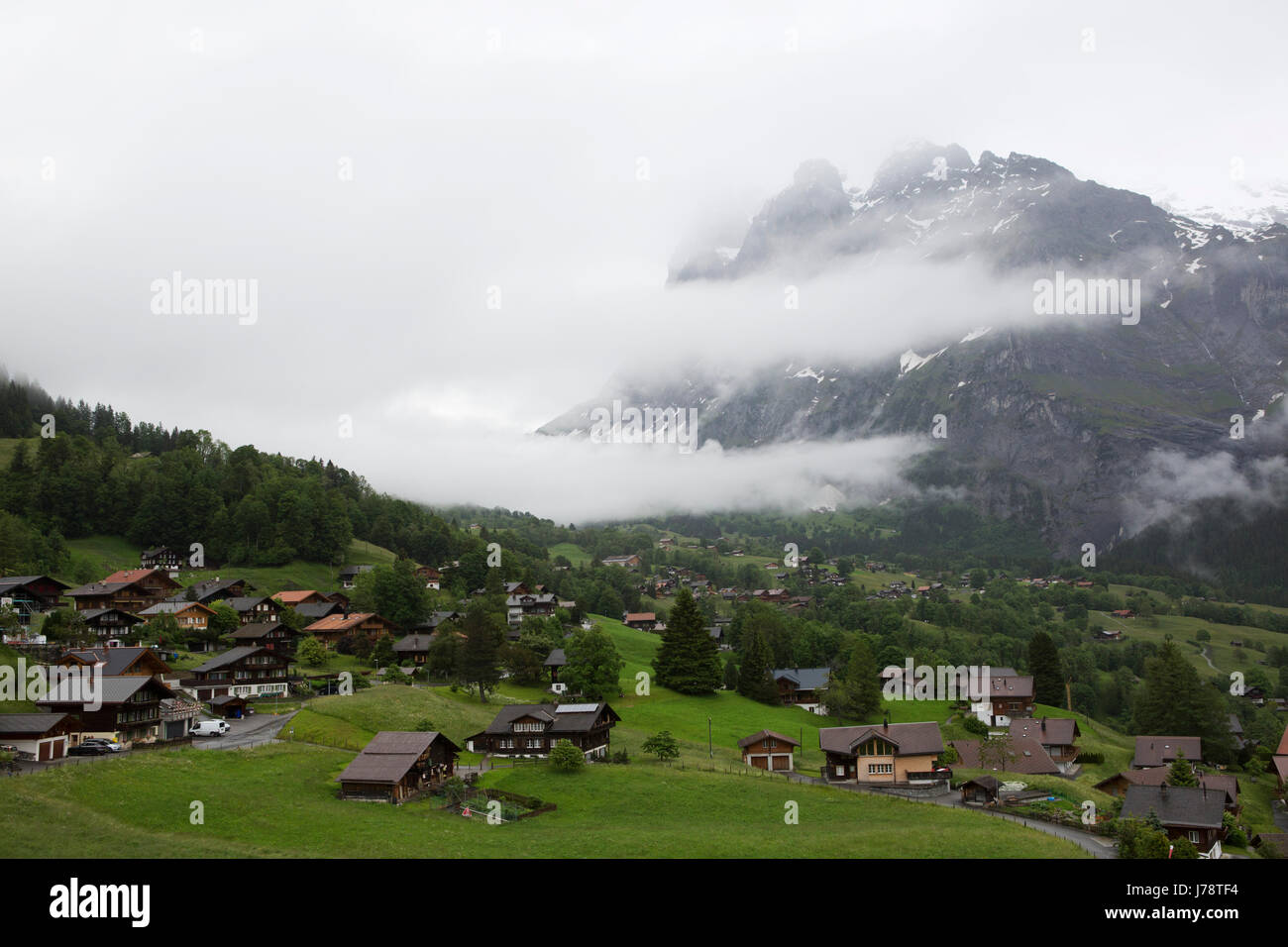 Nuvole mano sulle Alpi nella regione di Jungfrau della Svizzera. Chalets può essere visto nella valle. Foto Stock