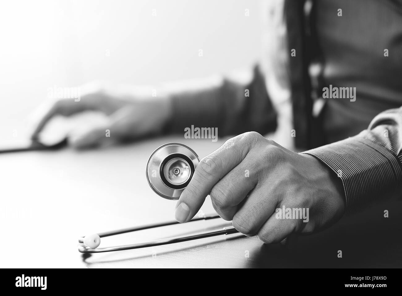 Chiudere smart medico lavora con lo stetoscopio e il telefono mobile in legno scuro, scrivania in ospedale moderno,in bianco e nero Foto Stock