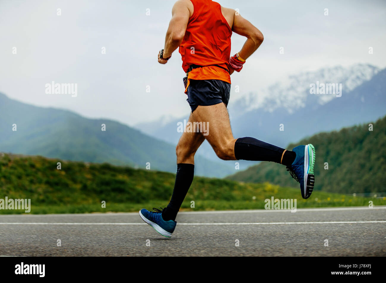 Uomo che corre atleta calze di compressione sullo sfondo delle montagne e foresta verde Foto Stock