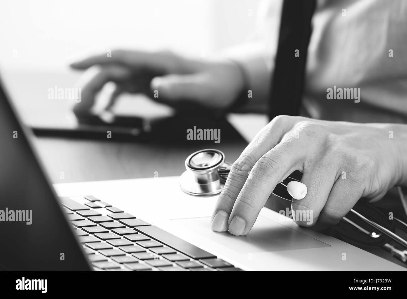 Chiudere smart medico a lavorare con il computer portatile e il telefono cellulare e lo stetoscopio in legno scuro, scrivania,in bianco e nero Foto Stock