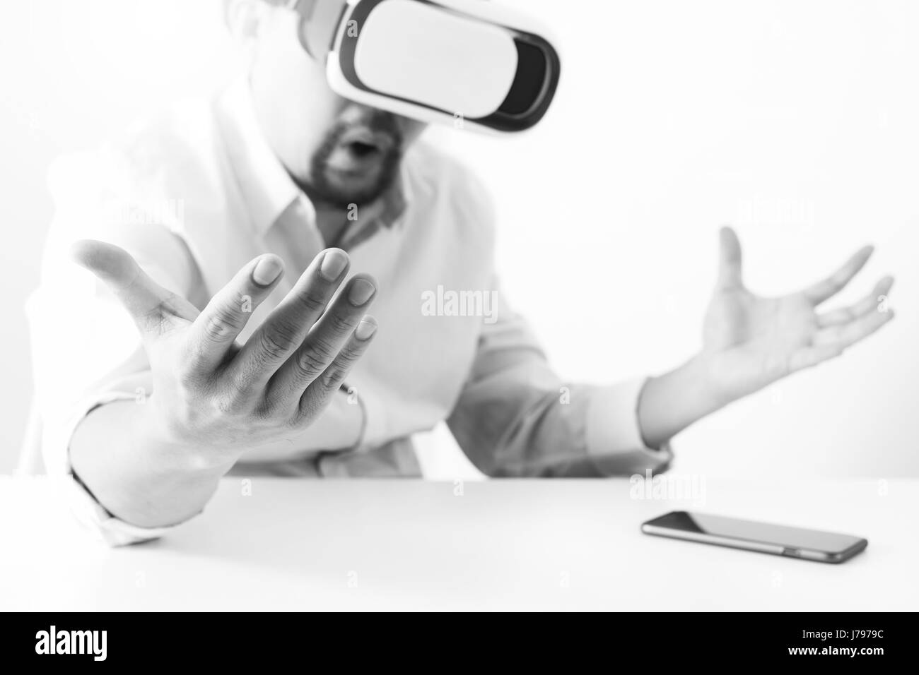 Imprenditore indossando la realtà virtuale gli occhiali di protezione in un ufficio moderno con lo smartphone utilizzando con VR auricolare,in bianco e nero Foto Stock