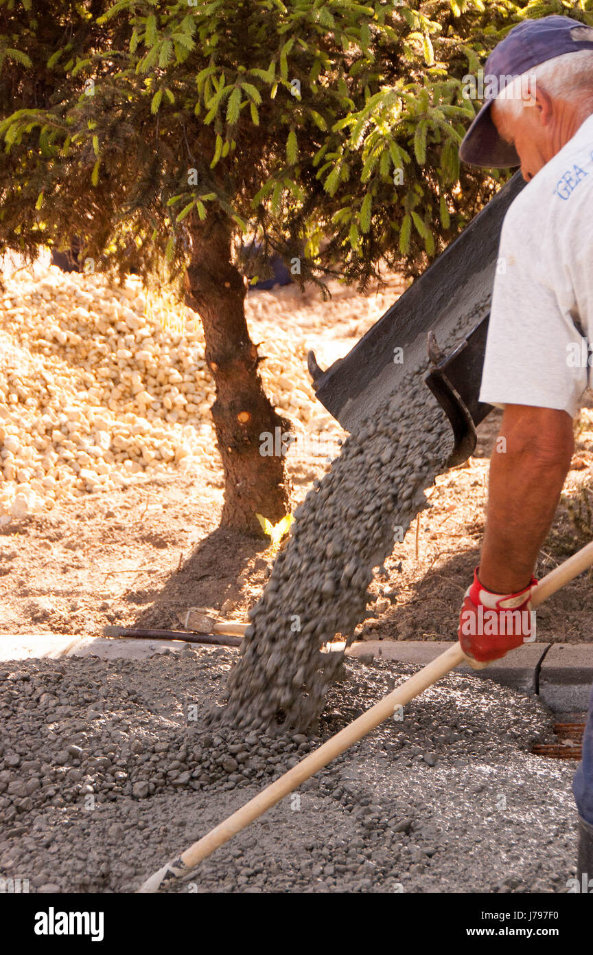 I lavoratori lavorano su cementificazione spazi di parcheggio davanti alla casa. Mason lavoratore in calcestruzzo di livellamento con le cazzuole mason mani diffondere la colata di calcestruzzo. Foto Stock