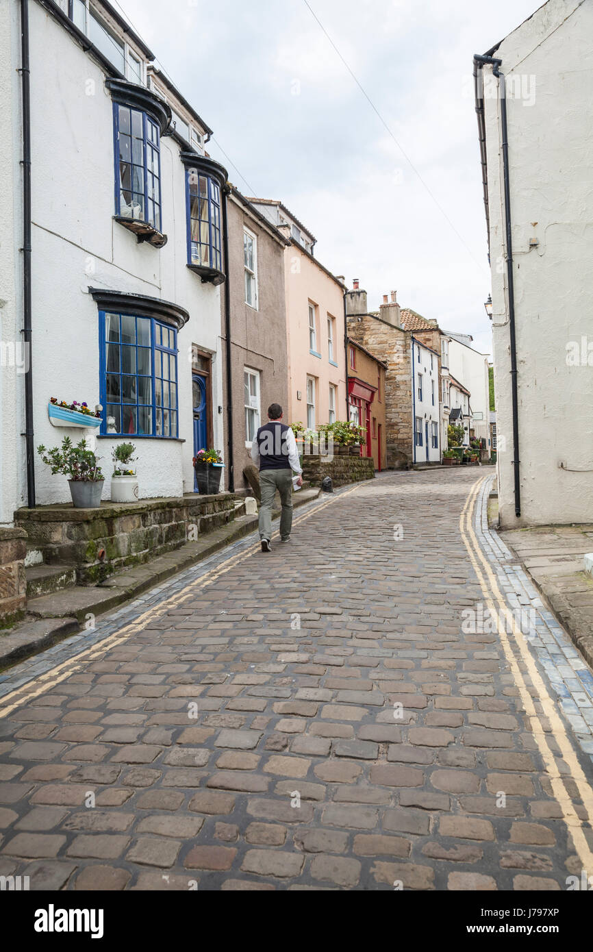 Un uomo cammina lungo le strade acciottolate e tortuose di Staithes, North Yorkshire, Regno Unito Foto Stock