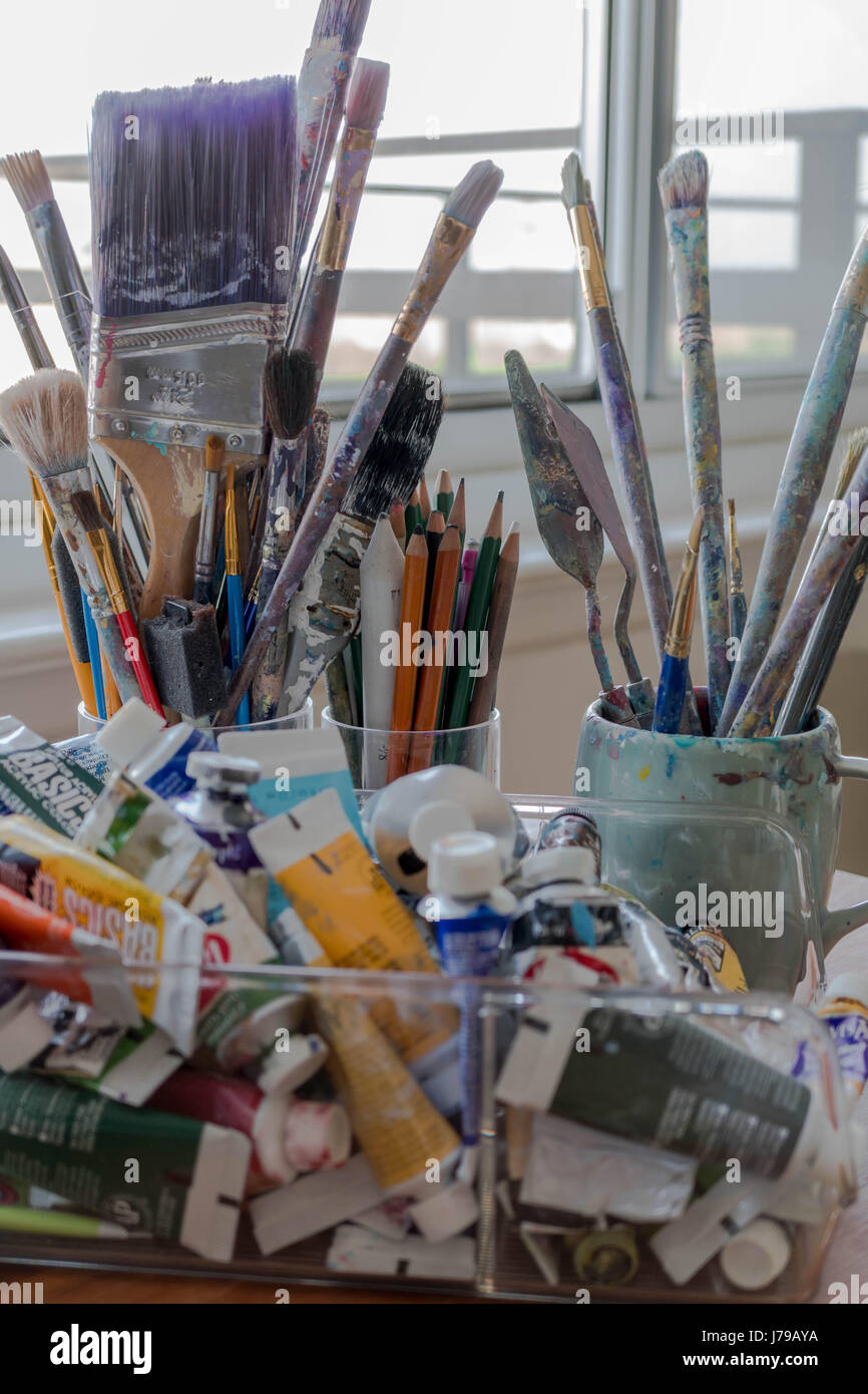 Artists Studio con pennelli, vernici, matite colorate, matite, una tavolozza di coltelli e altri materiali di consumo di arte di fronte a una finestra Foto Stock