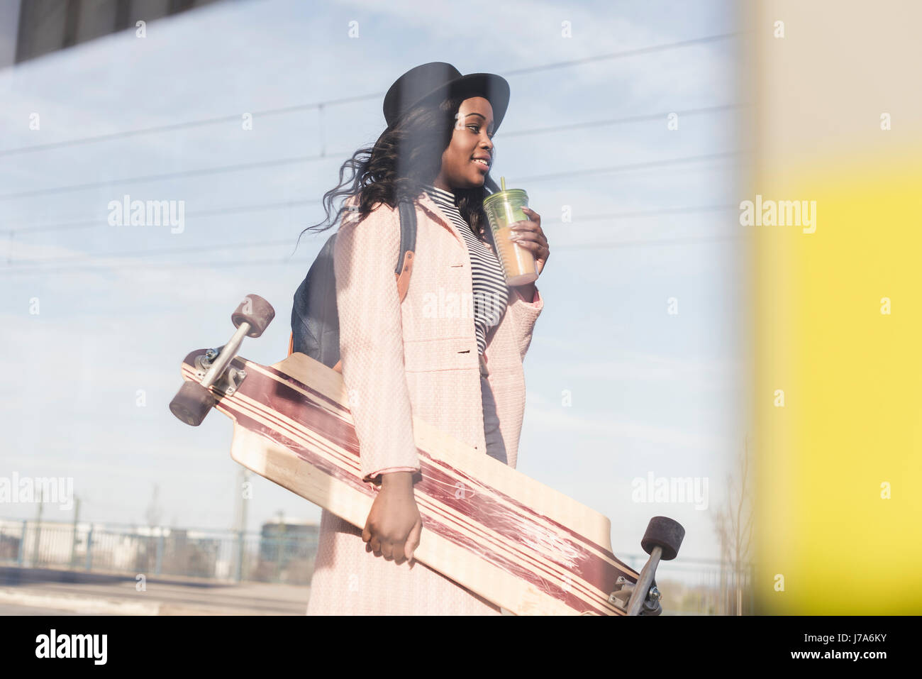 Giovane donna che trasportano skateboard, drining dalla tazza monouso Foto Stock