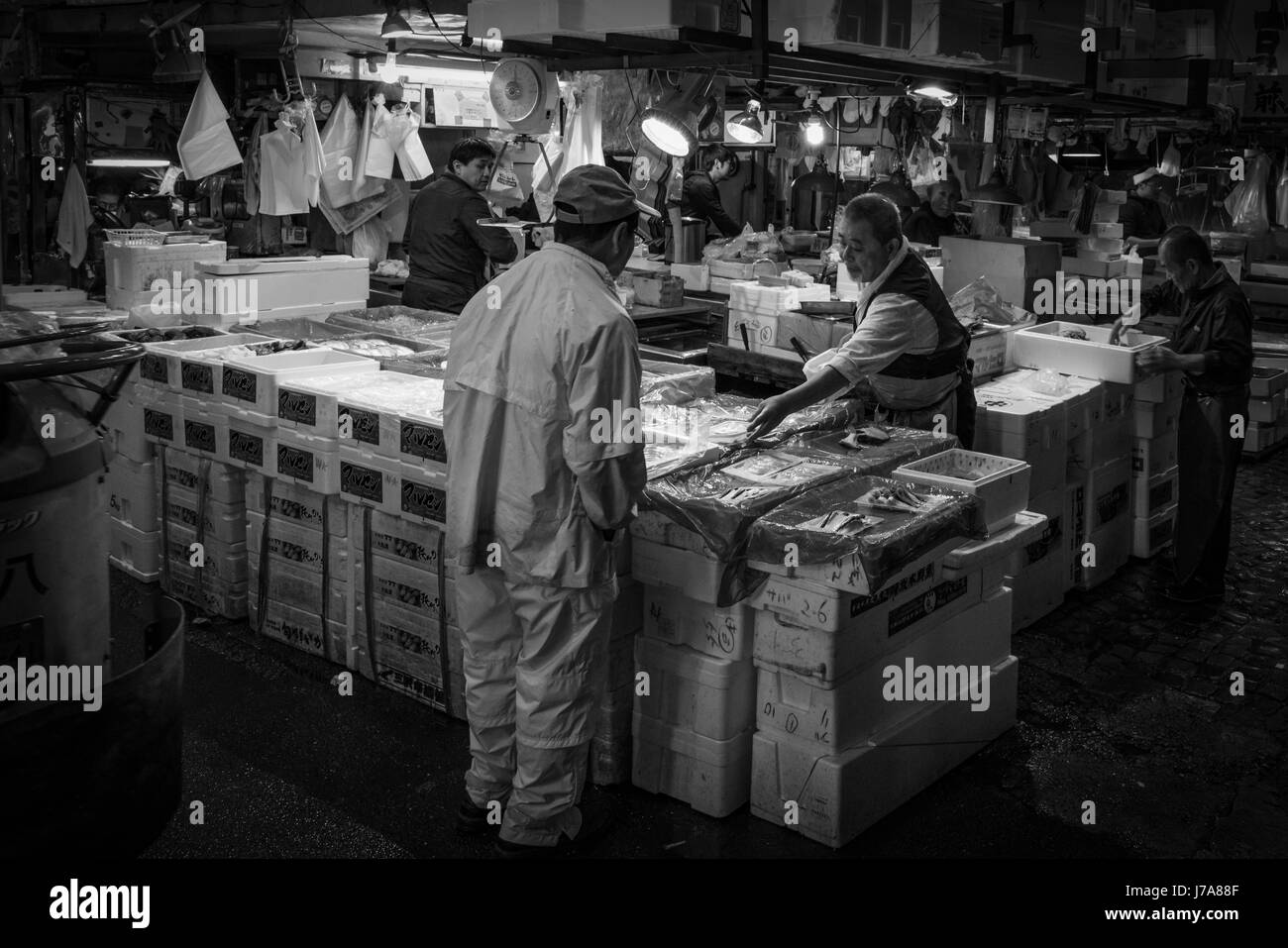 Foto in bianco e nero del mercato del pesce Tsukiji con molti uomini giapponesi occupato a gestire e mettere il pesce in grandi scatole di polistirolo da caselle. Foto Stock
