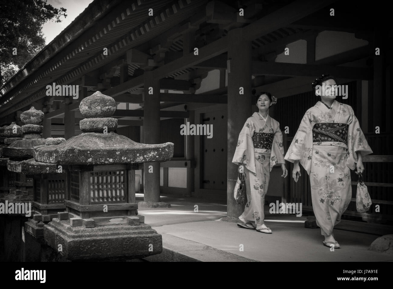 Foto in bianco e nero di due giovani donne che indossano i loro furisode di Nara. Sono passato di risveglio alcune lanterne di pietra. Foto Stock