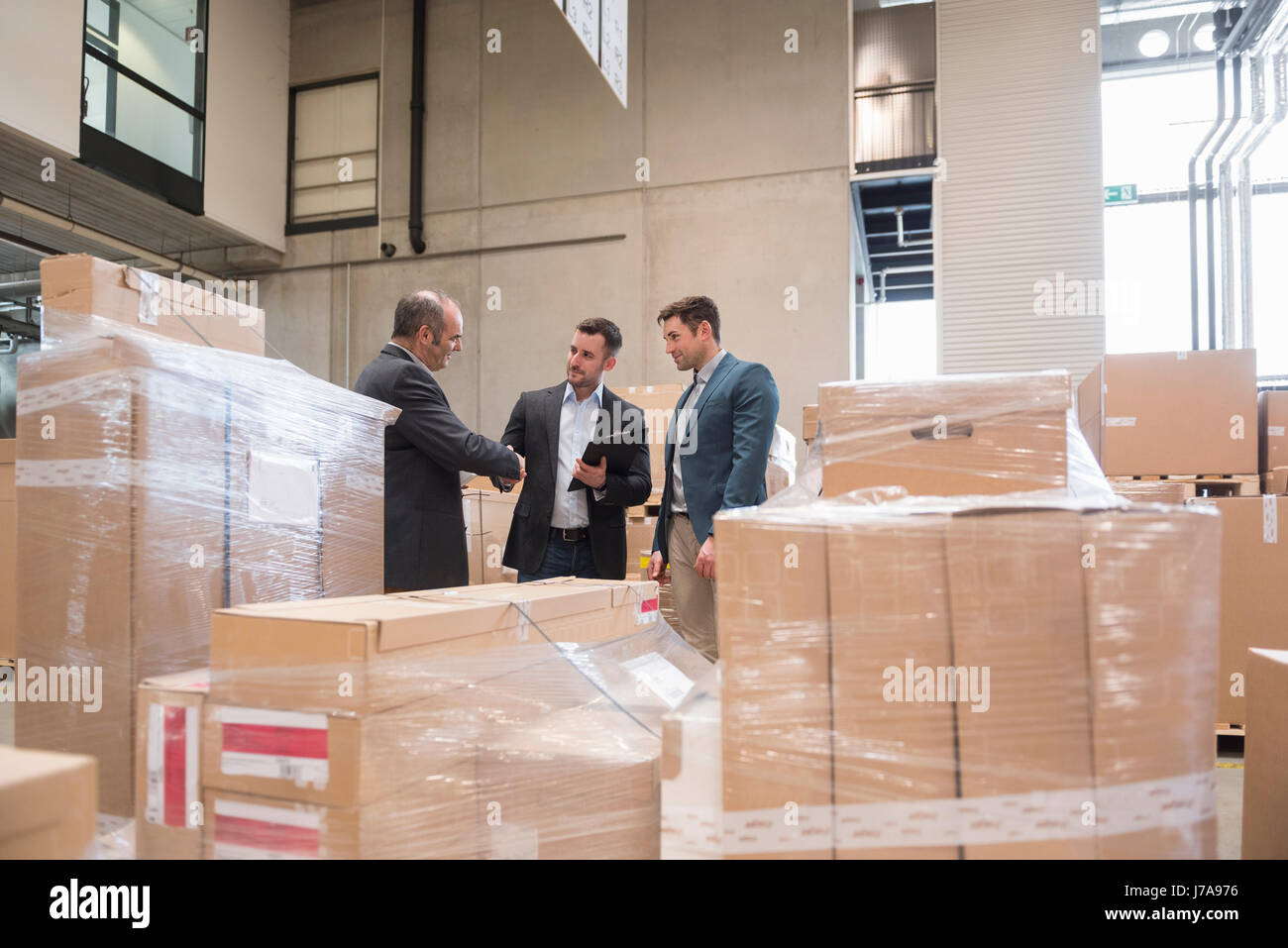 Tre uomini in magazzino di fabbrica circondato da scatole di cartone Foto Stock