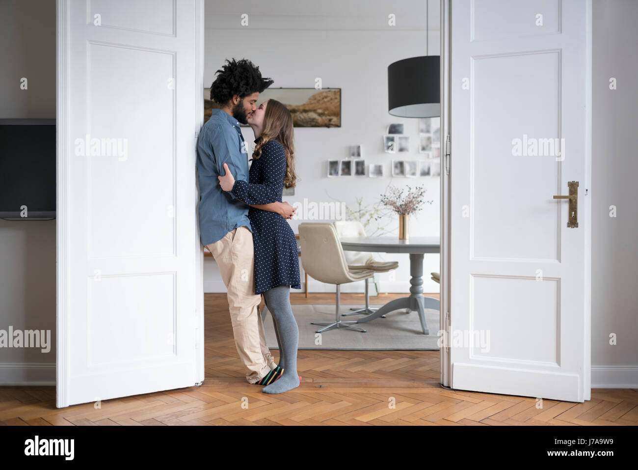 Kissing giovane a casa in piedi nel telaio della porta in soggiorno Foto Stock