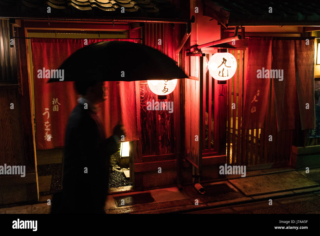 Uomo con ombrello passeggiate passato una casa da tè (ochaya), nel quartiere di Gion. Le luci portano la vita per strada di notte Foto Stock