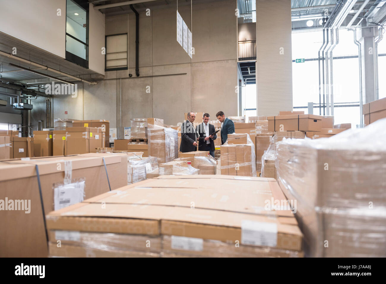 Tre uomini in magazzino di fabbrica circondato da scatole di cartone Foto Stock