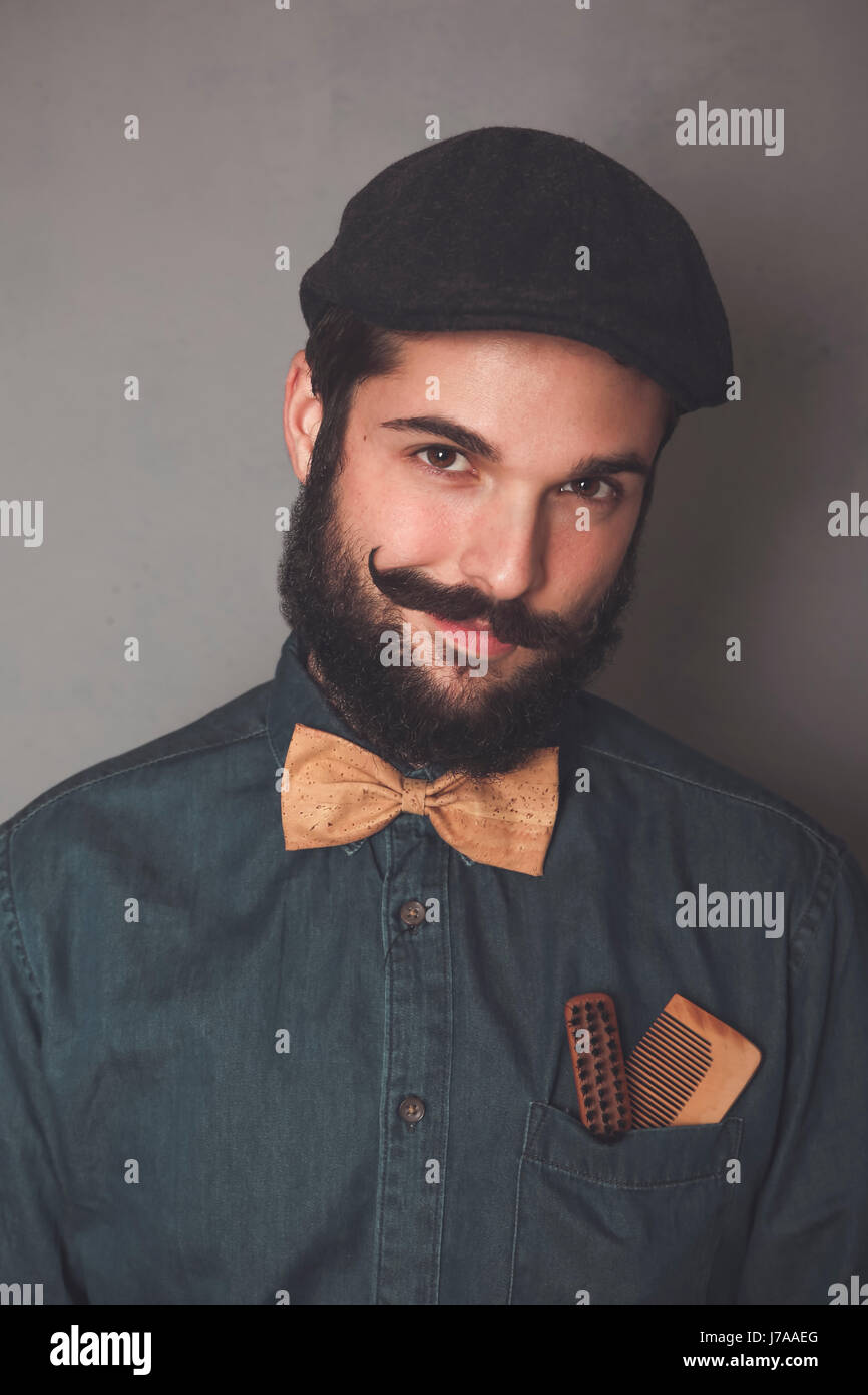 Ritratto di uomo barbuto che indossa il cappuccio, denim shirt, sughero bow tie, indossando i pettini in legno per la barba e baffi in tasca Foto Stock