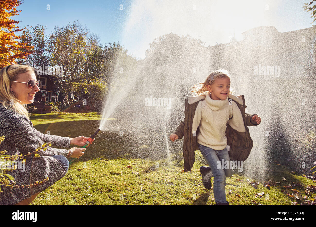 Madre e figlia giocando con il tubo da giardino in autunno Foto Stock