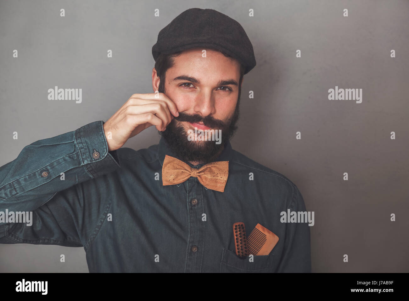 Ritratto di uomo barbuto che indossa il cappuccio, denim shirt, sughero bow tie, indossando i pettini in legno per la barba e baffi in tasca Foto Stock