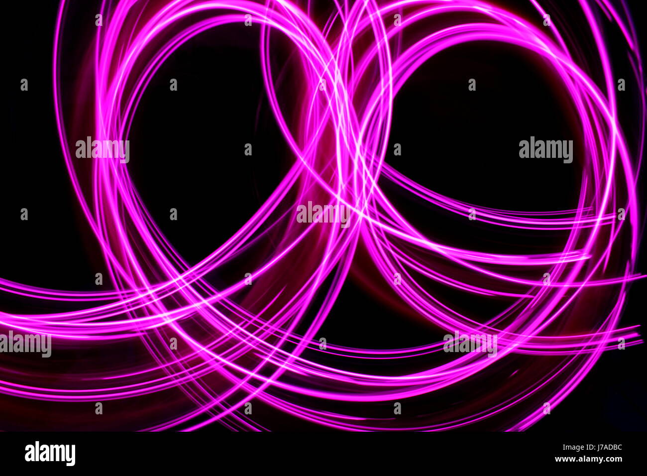 Una lunga esposizione fotografia di neon di colore rosa in un abstract loop modello contro uno sfondo nero. Luce fotografia pittura, di colore in astratto Foto Stock