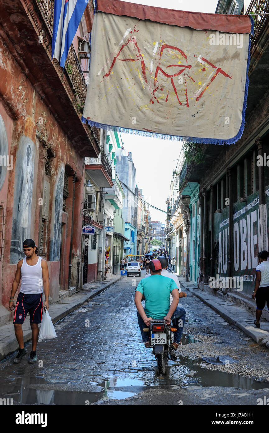 Scena di strada a l'Avana, Cuba. Un ciclomotore da parte di guida sotto appeso un poster Foto Stock