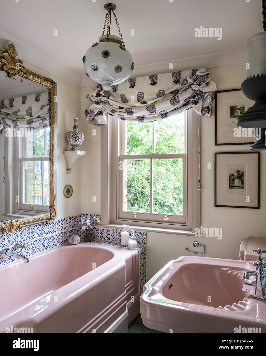 Rosa ghisa smaltata vasca da bagno e lavandino in bagno con terra cotti piastrelle e ornati specchio dorato Foto Stock