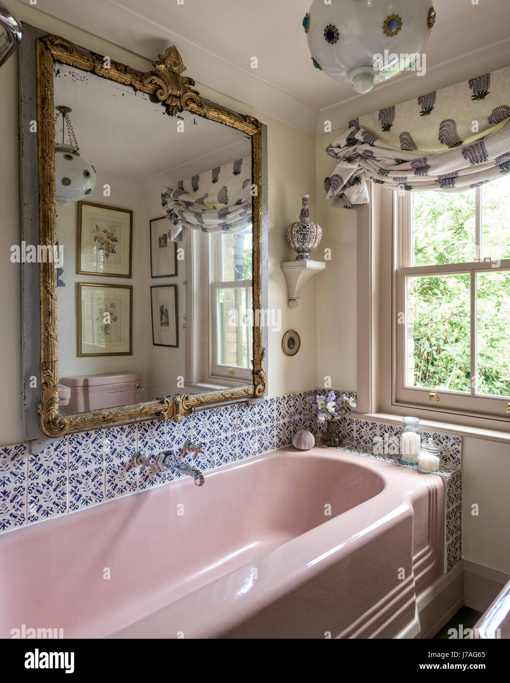 Rosa ghisa smaltata vasca da bagno e lavandino in bagno con terra cotti piastrelle e ornati specchio dorato Foto Stock