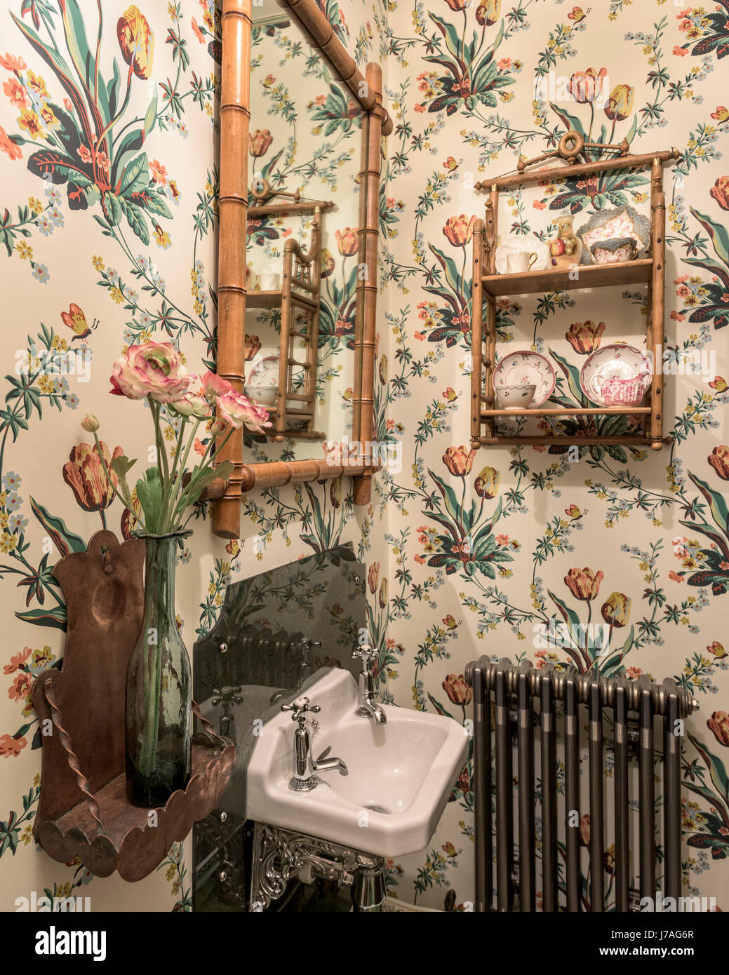 Carta da parati floreale nel guardaroba con termosifone in ghisa e bambù specchio incorniciato Foto Stock